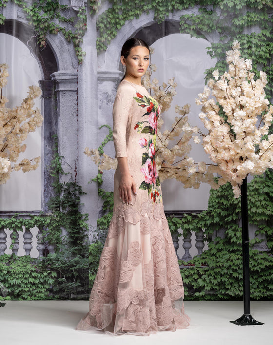 Woman wearing a modest blush pink floral gown with a colorful floral and strawberry design on the front and three quarter sleeves.