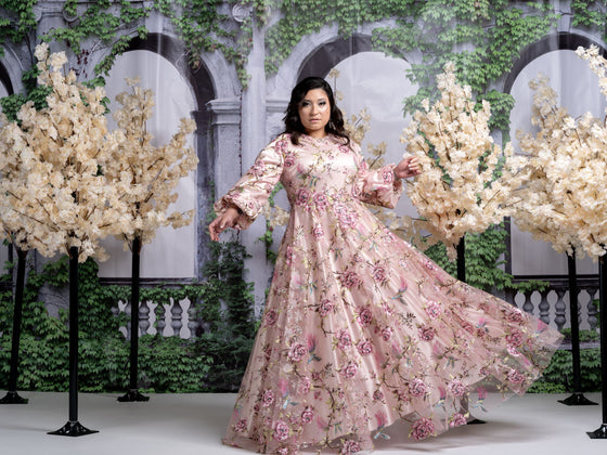 Plus size woman wearing a light pink modest gown with a floral and bird print.