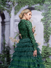 A woman wearing a modest ombre green tiered gown with long sleeves. The gown has a fitted bodice and multiple tiers of ruffles.