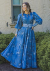 Woman wearing a dusty blue chiffon floral modest gown. The gown has volumnious puff sleeves and blue floral lace detailing at the waist and cuffs. 