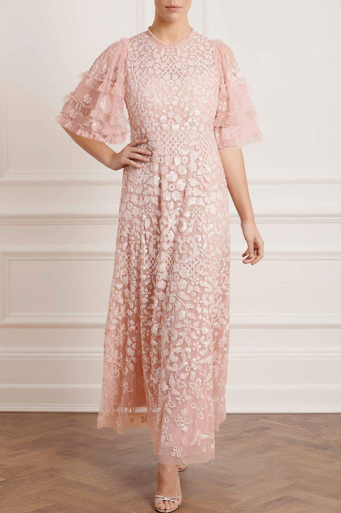 Woman wearing modest Needle & Thread Aurelia Gown in pink strawberry icing color. The gown is adorned in light pink sequin detailing and has three-quarter flare sleeves.