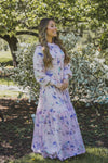 A woman wearing a modest light pink gown with lilac florals and a large ruffle hem.