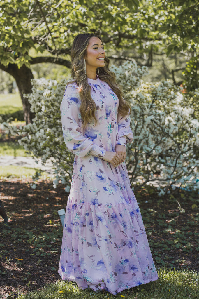 A woman wearing a modest light pink gown with lilac florals and a large ruffle hem.