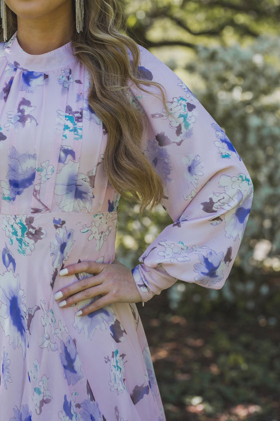 A woman wearing a modest light pink gown with lilac florals and a large ruffle hem.