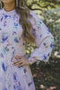 A woman wearing a modest light pink gown with lilac florals and a large ruffle hem.