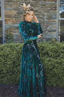  Woman wearing modest dark green floral velvet burnout gown with long sleeves that feature slight puff at the shoulders and a high collar neck. 