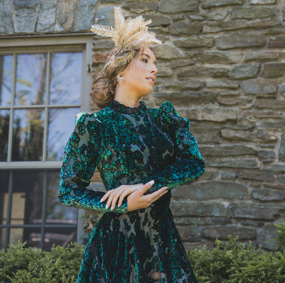 Woman wearing modest dark green floral velvet burnout gown with long sleeves that feature slight puff at the shoulders and a high collar neck. 