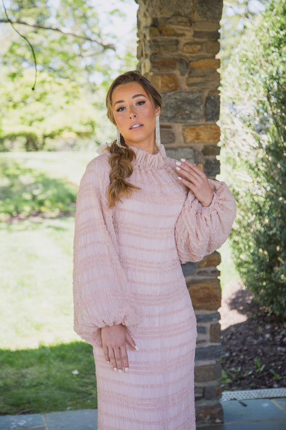 A woman wearing a light, delicate blush pink modest gown with voluminous sleeves and a high neck. 