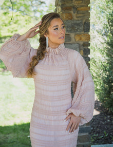  A woman wearing a light, delicate blush pink modest gown with voluminous sleeves and a high neck. 