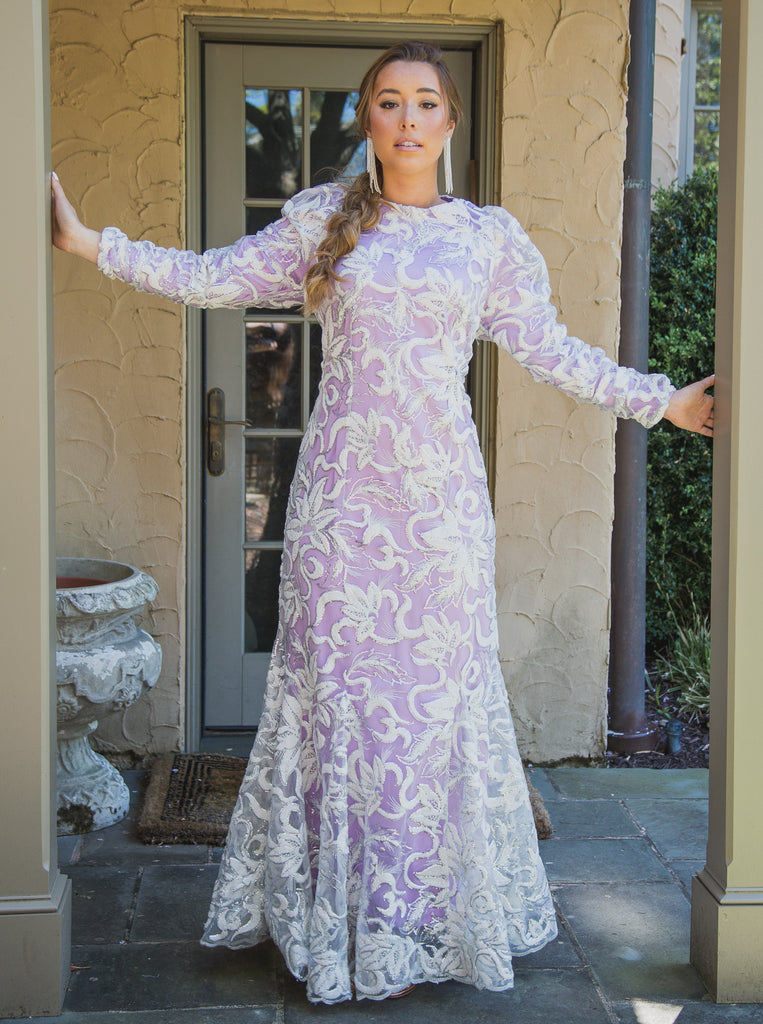 A woman wearing a modest purple chenille gown.  The gown has long sleeves with a slight puff at the shoulder adding a touch of drama and elegance. 