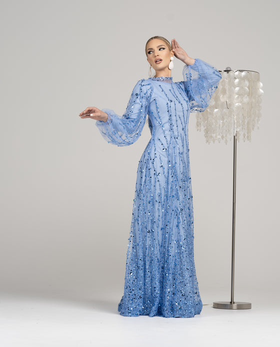 A woman wearing a blue sequined modest evening gown with billowing sleeves. The gown is adorned with sparkling sequins that catch the light, giving it a sophisticated and elegant look. 