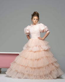  A girl wearing a modest blush pink ball gown with puff sleeves and a floral top. The gown has a tiered ball gown skirt.