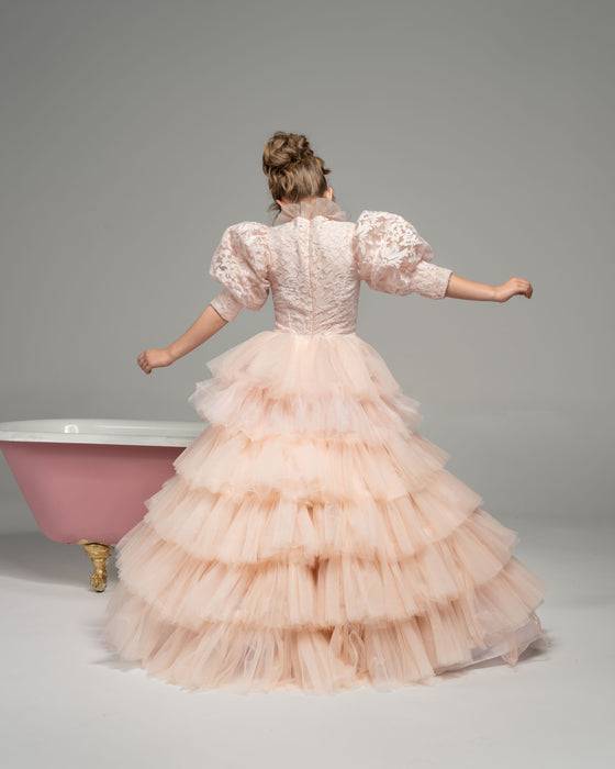 A girl wearing a modest blush pink ball gown with puff sleeves and a floral top. The gown has a tiered ball gown skirt.