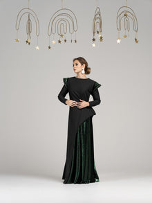  A woman wearing a modest green straight, long sleeve evening gown. The gown features a unique combination of green velvet on half of the skirt and green velvt shoulder detailing.