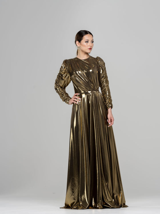 A woman wearing a golden ruched gown with long sleeves. The gown has a fitted bodice and a flowing skirt.