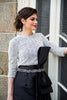 A woman wearing a modest black & white gown with a large bow by the waist. The gown has a pearl Italian fabric top paired with a taffeta structured bold ballgown skirt with asymmetrical lines. The gown has three-quarter sleeves and a crew neck.