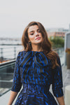 Woman wearing modest cobalt blue and black ball gown with cropped bolero. The three-quarter sleeve bolero has a large bow detail in front and mini covered buttons cascading down the back.