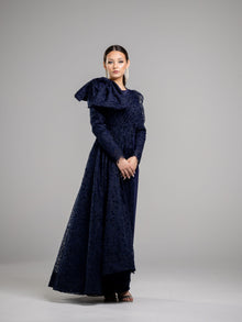  A woman wearing a modest navy lace gown with  long sleeves. The gown features a large bow on one shoulder. 