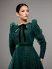 Woman wearing an elegant dark green gown with velvet polka dots, a bottom tier and a green velvet bow at the neck. 