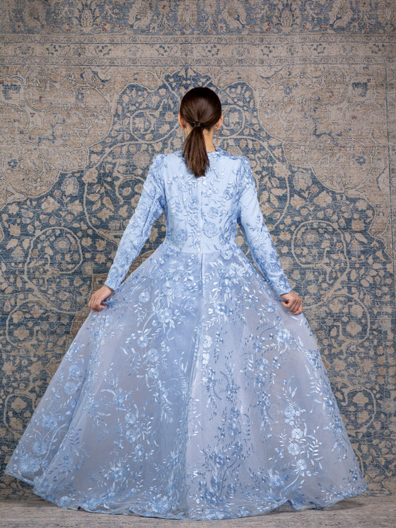 Woman wearing a modest powder blue floral long sleeve gown with a flowing skirt cape for added elegance.