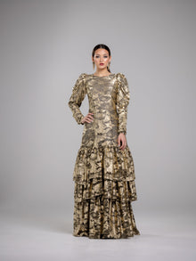  A woman wearing a modest gold floral pattern gown with voluminous sleeves. The gown has a fitted bodice and a flowing skirt with three tiers of ruffles. 