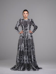  A woman wearing a black and white floral guipure open lace modest evening gown with long sleeves. 