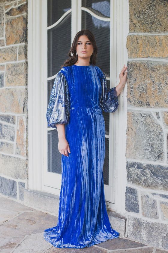 Woman wearing modest cobalt blue crushed velvet ruched gown with straight silhouette and billowy three-quarter length sleeves.