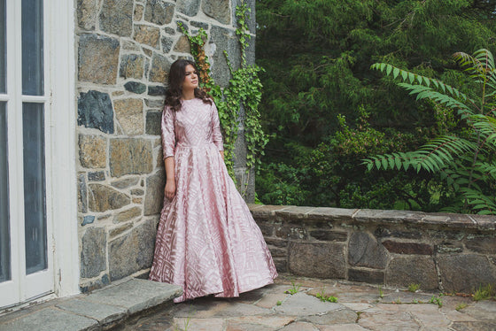 Woman wearing a modest blush pink ball gown with pink foiled geometric shapes and three-quarter length sleeves.