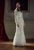 Woman wearing a modest ivory Needle & Thread gown.  The gown is crafted from vintage tulle and lace and adorned with intricate beaded embellishments.  It has a fitted bodice, fluted sleeves and a floor sweeping hem.